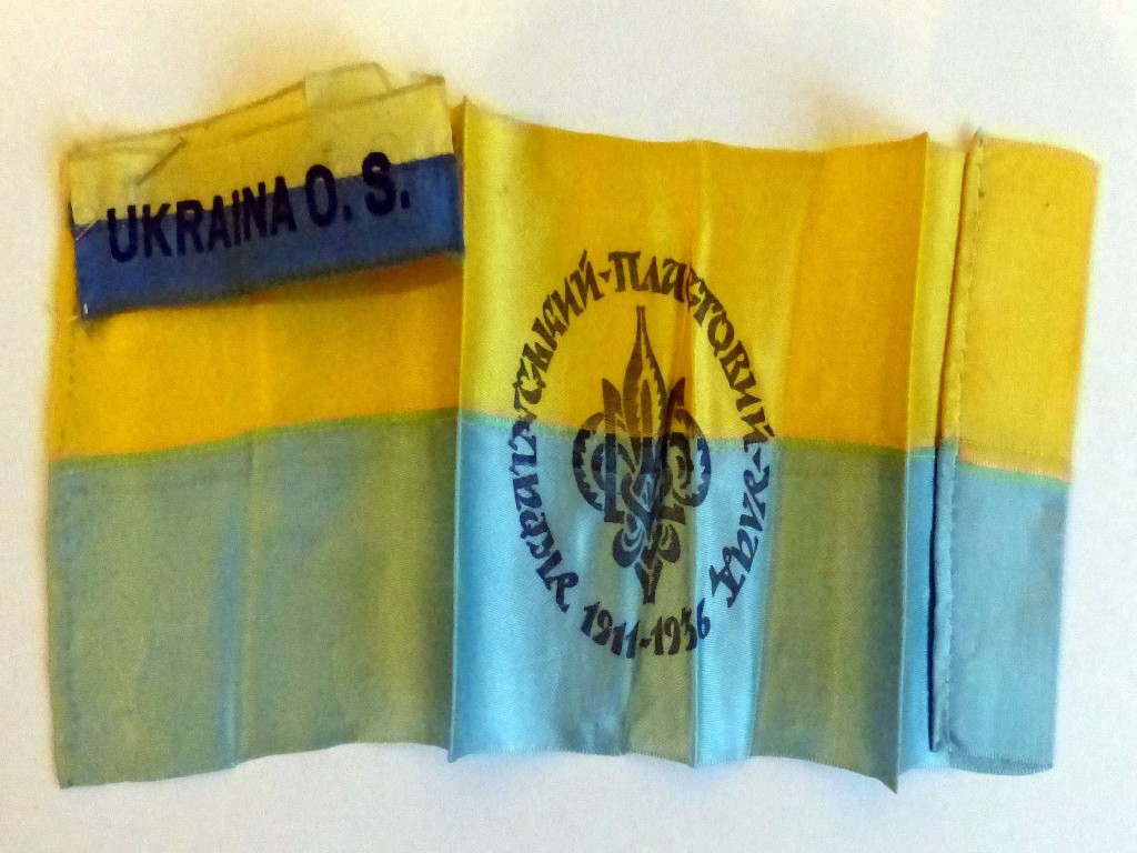 Жовто-блакитний прапор з атласу із зображенням герба Пласту (у вигляді Тризуба, переплетеного з трилистою лілеєю) і написом “Український пластовий улад 1911-1926” та дві стрічки з жовто-синього атласу з написом ”UKRAINA O. S.” 